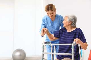 Foto: Pflegekraft hilft älterer Frau mit Gehhilfe